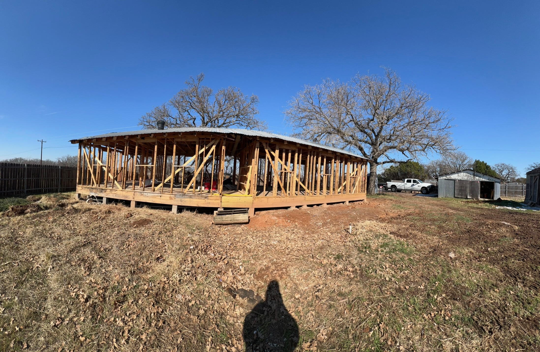 A wide view of the back of the lot with a large oak tree, snow patches on bare dirt, and open sky.