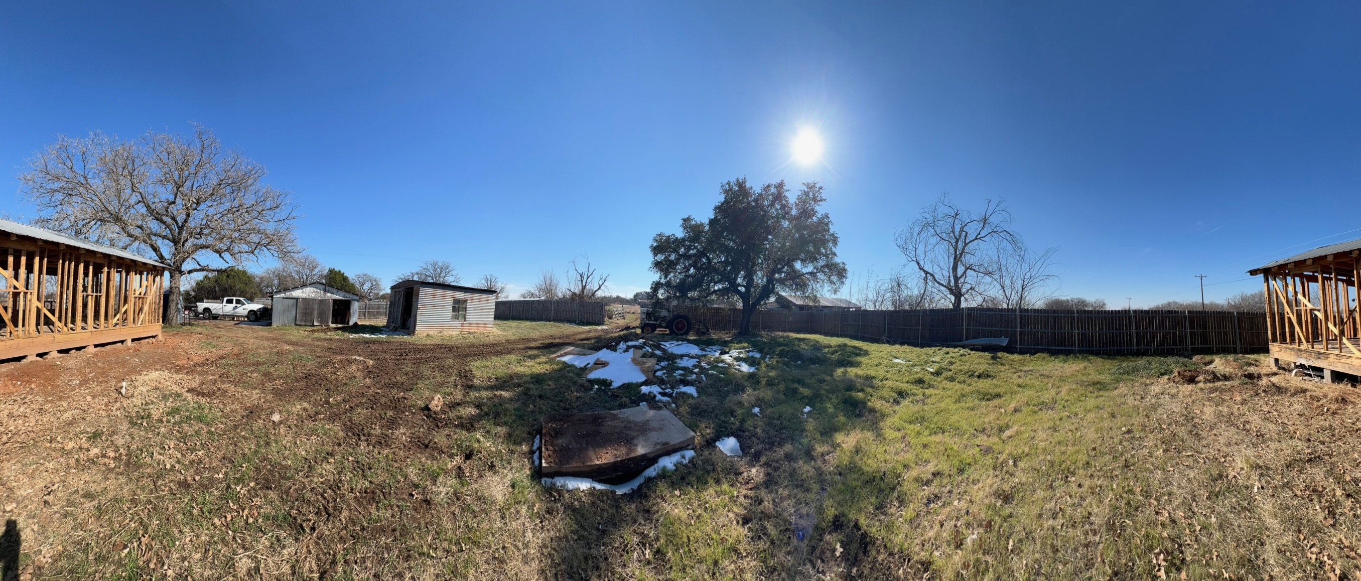 Panoramic view of the lot showing existing framing, fencing, mature trees, and open yard.
